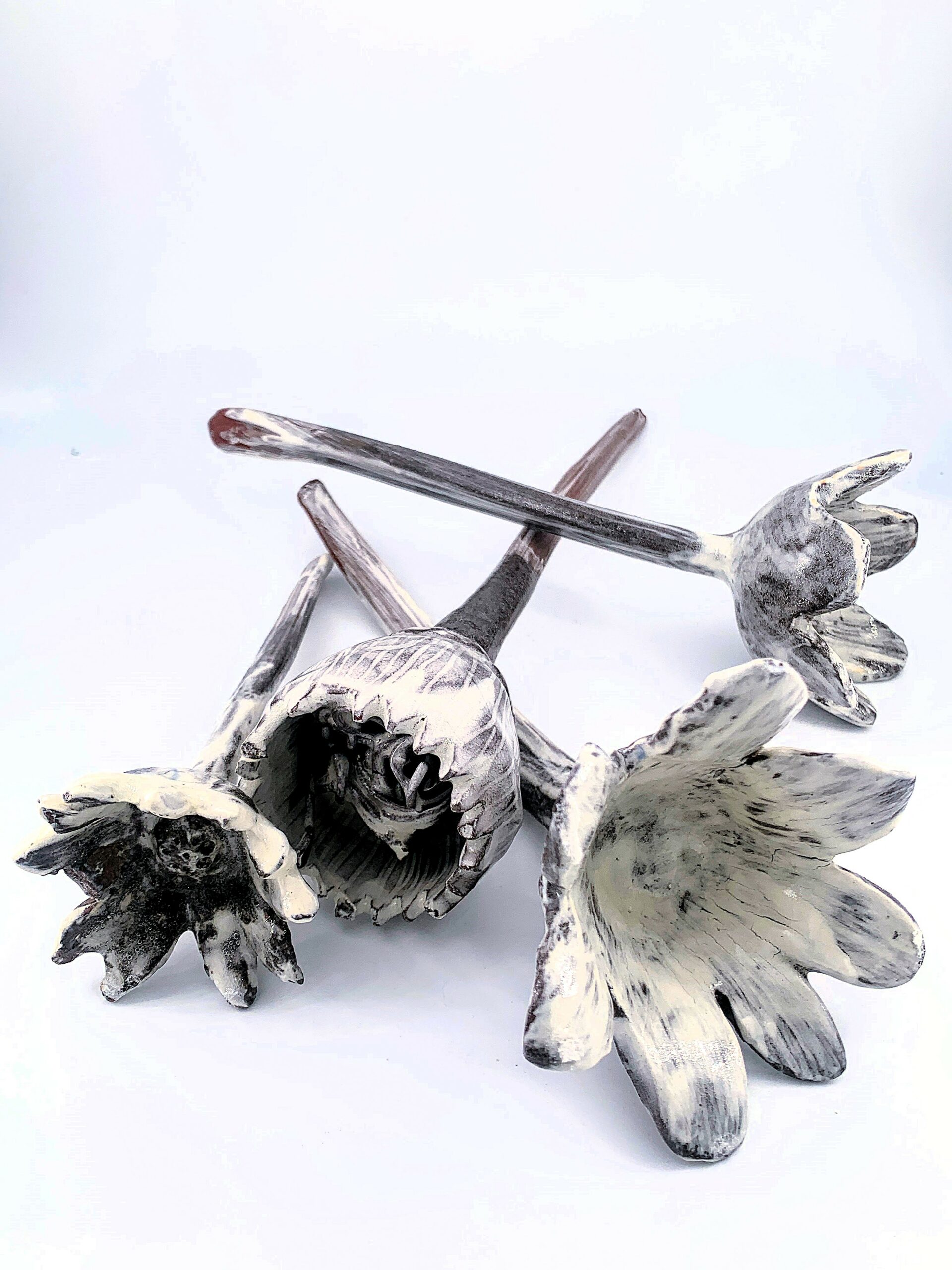 FLEURS, 2026, Grès rouge, engobe de porcelaine et glaçure transparente, longueur 17 à 27 cm, corolles Ø 8–9 cm, cuisson électrique, 1280 °C Quatre fleurs en grès rouge, recouvertes d’engobe de porcelaine et de glaçure transparente, aux tiges fines et courbes.