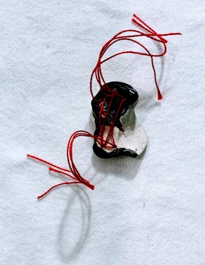 Forme noire et blanche composée de plusieurs volumes arrondis, reliés par un fil rouge qui serpente entre les éléments.