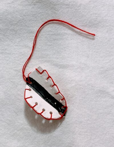 Petite forme blanche et noire, bordée de points de couture rouges et traversée par un fil rouge qui se prolonge au-delà de la pièce.